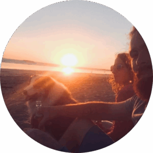 Un couple assis sur la plage au coucher du soleil avec leur chien, moment chaleureux et complice en bord de mer.